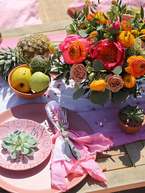 Summer table setting with pink and orange bouquet, fruit, succulents, and pink plates on a wooden table
